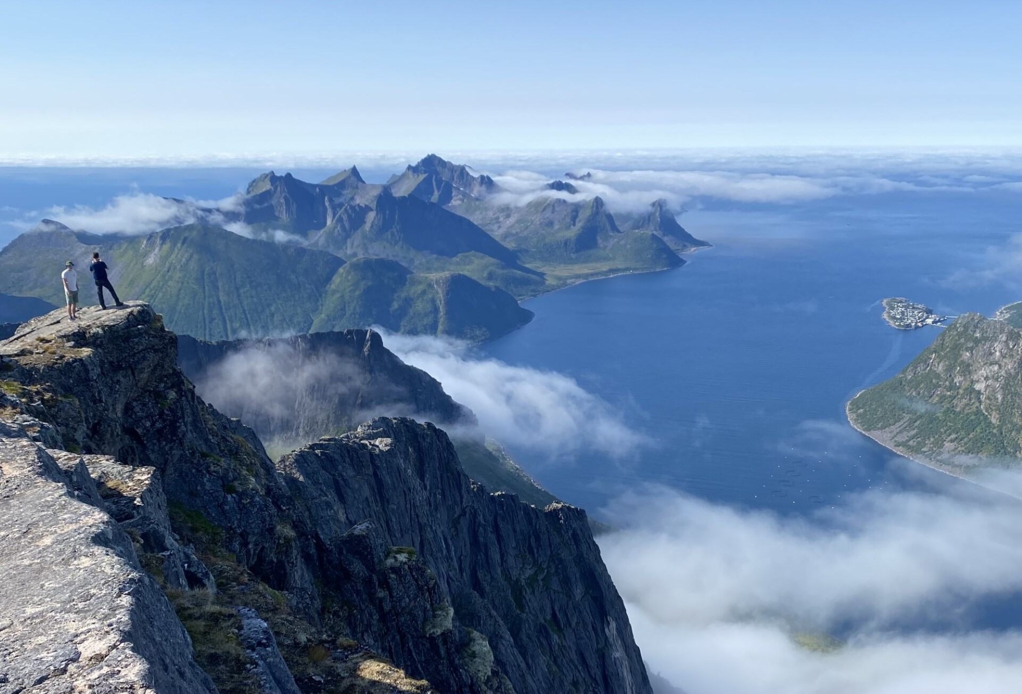 To menn står på en fjelltopp og ser utover fjell, fjord og Husøy i Senja