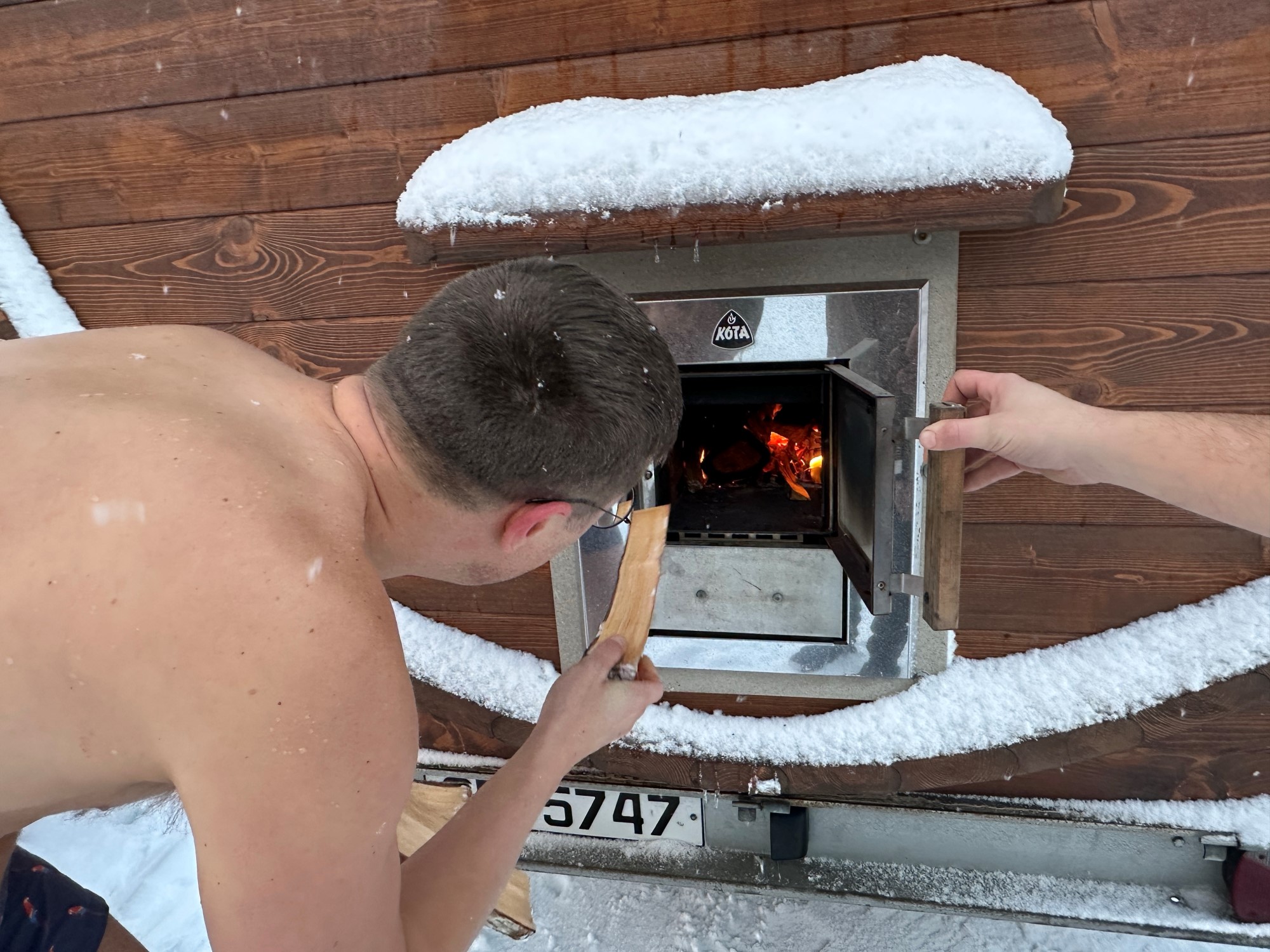 Bildet viser en mann som legger ved inn i ovnen til en badstu