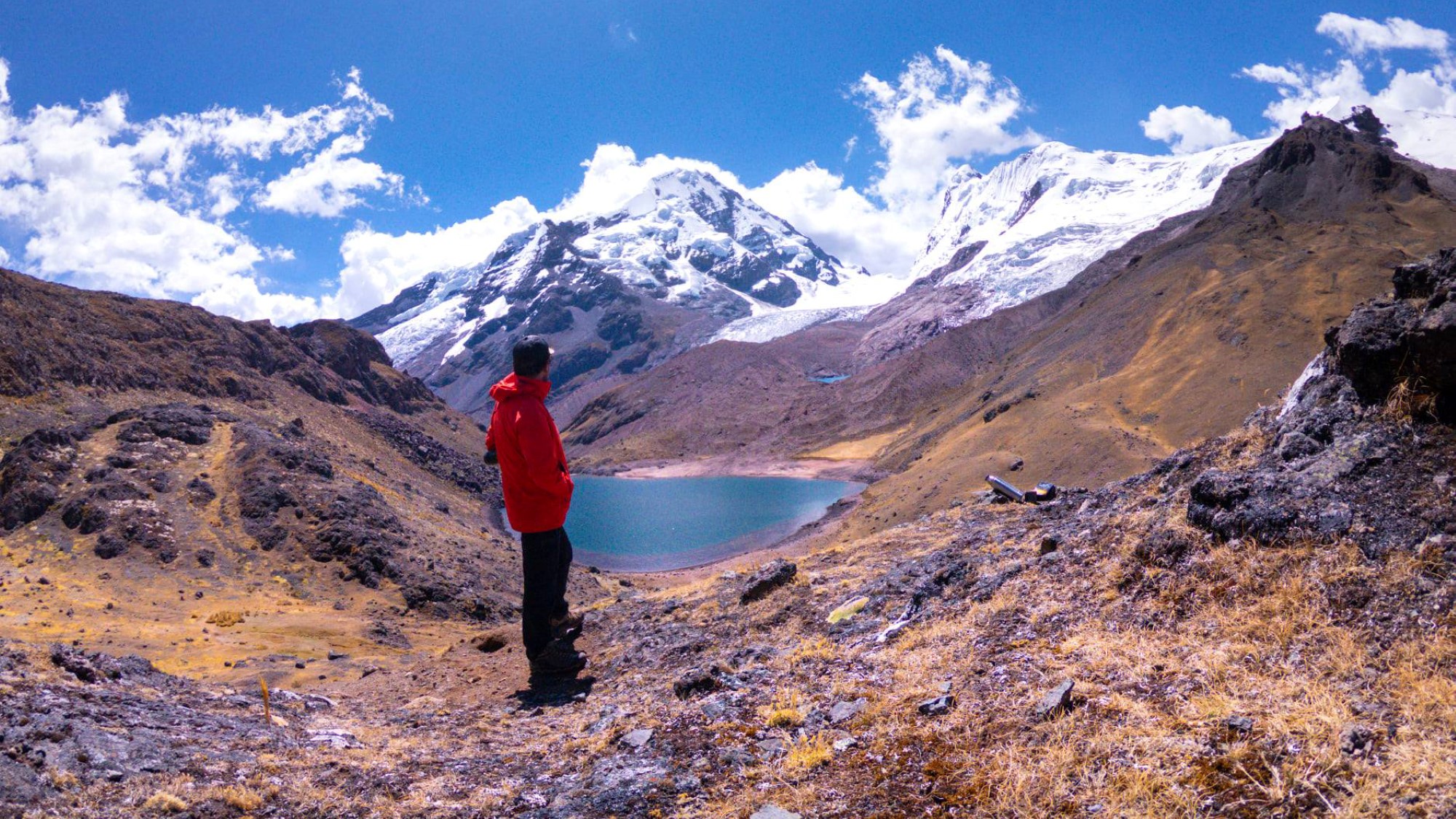 Mann i turklær ser utover liten innsjø i goldt fjellandskap i Andesfjellene