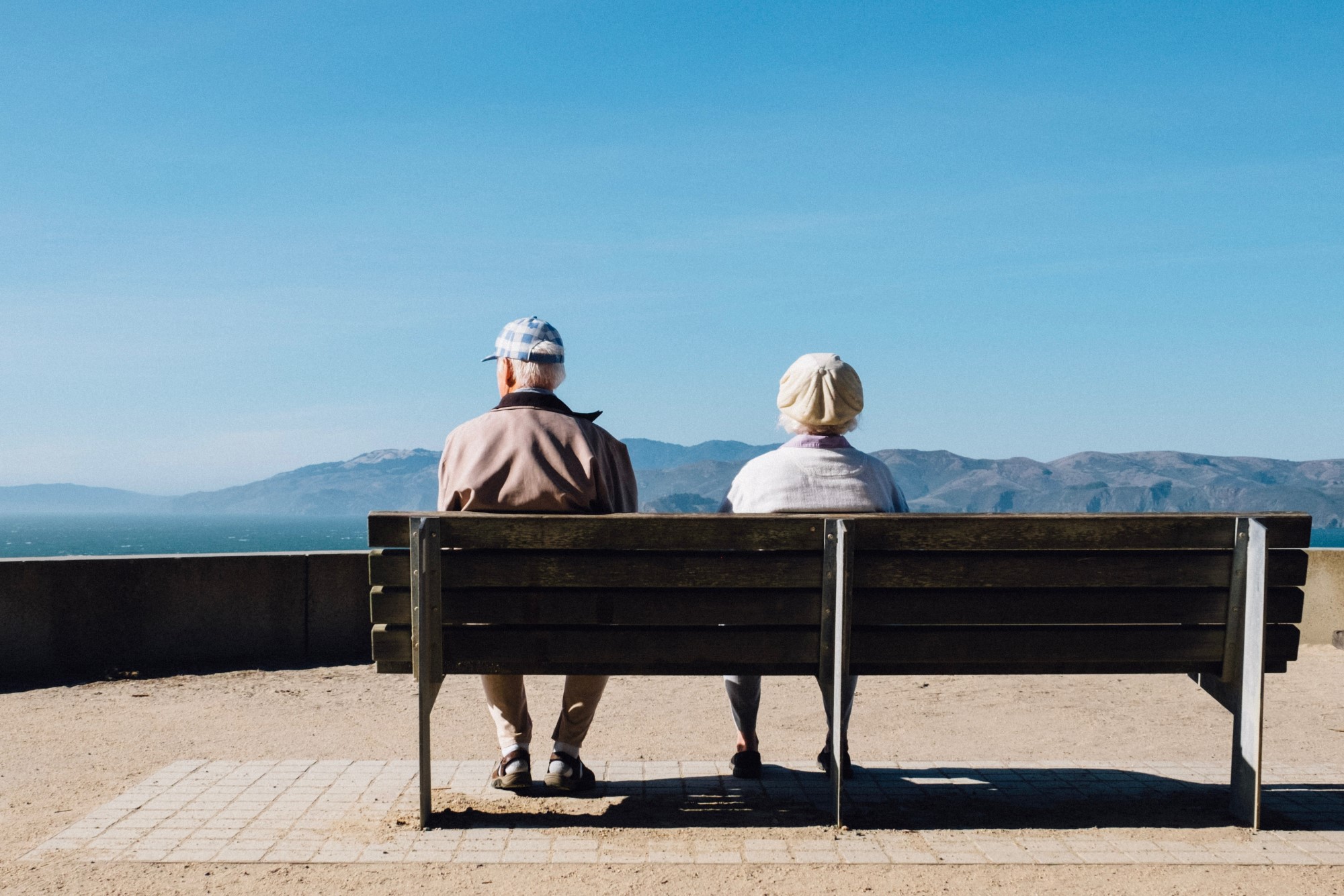Eldre mann og eldre kvinne sitter på benk og ser utover havet