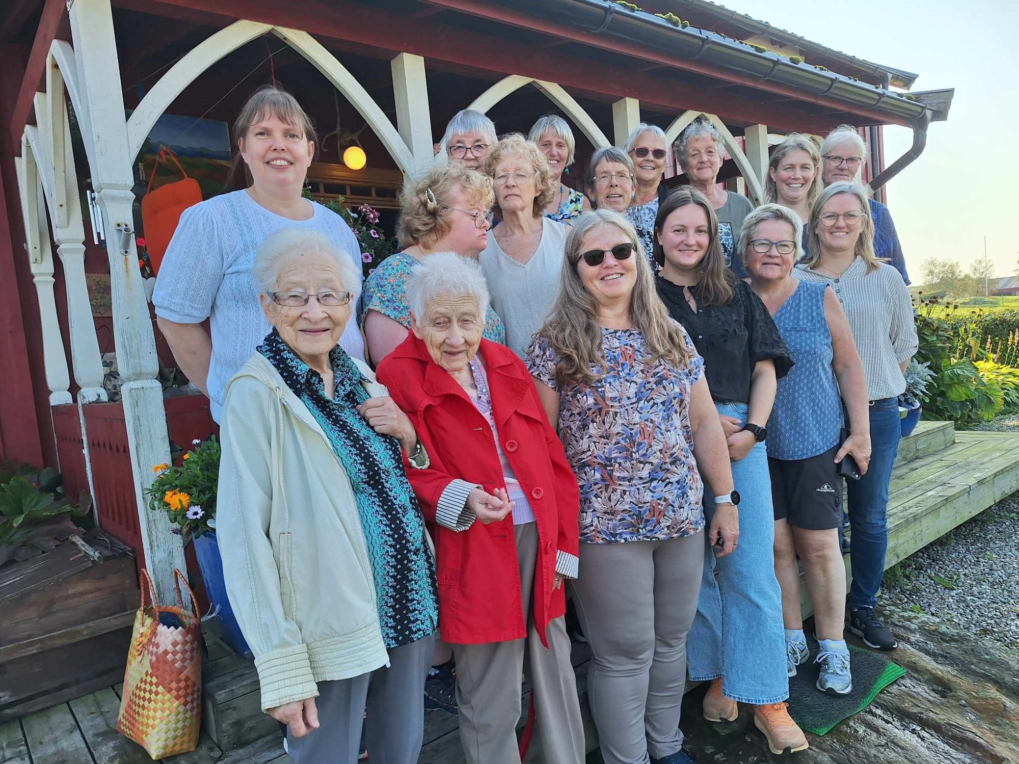 En gruppe smilende unge og eldre damer samlet foran rødt hus