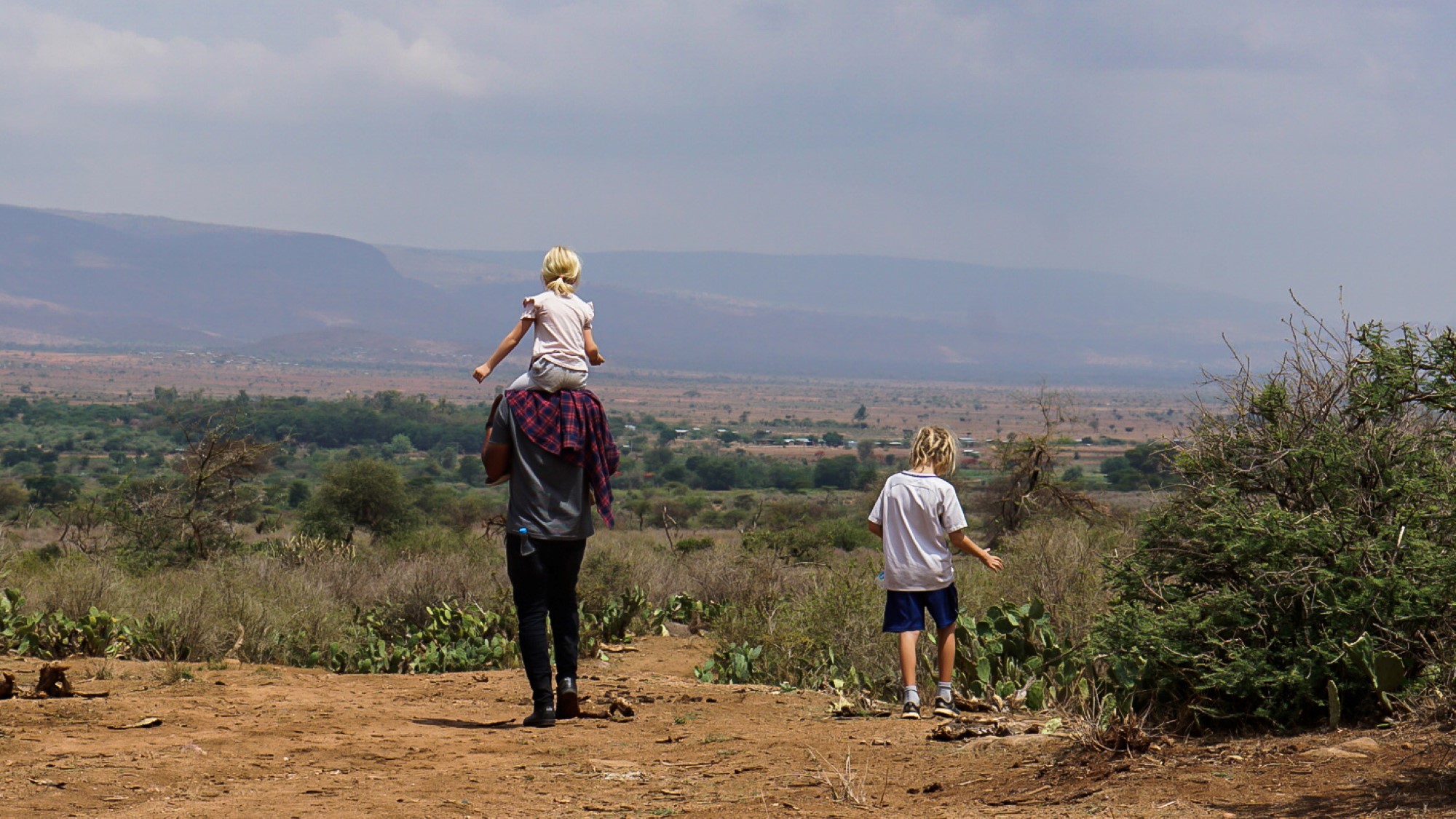 Far og to barn går tur i afrikansk savanne-landskap