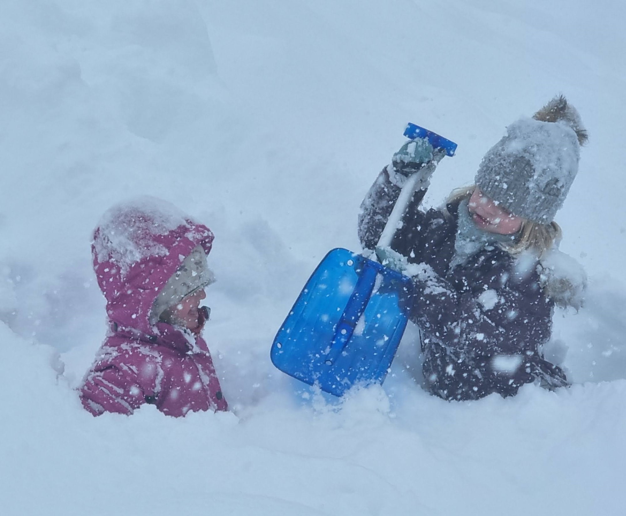 To jenter graver med spade i dyp snø