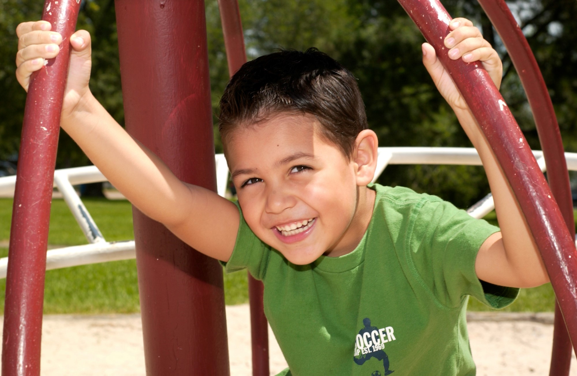 Smilende gutt i grønn skjorte som sitter i et lekestativ