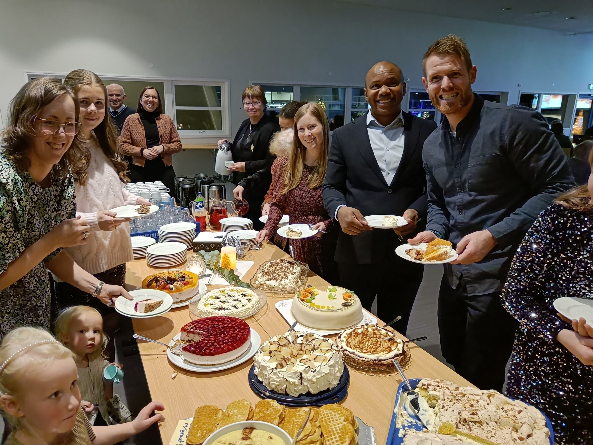 Bildet viser glade mennesker rundt et kakebord