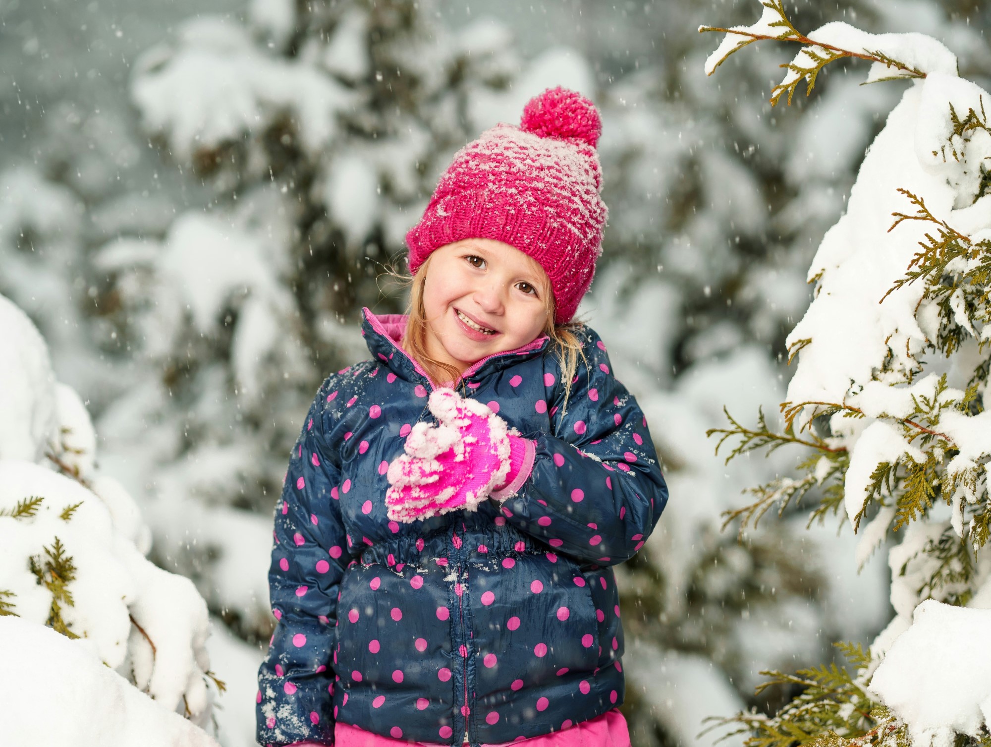 Jente med rosa lue som står i en snødekt skog