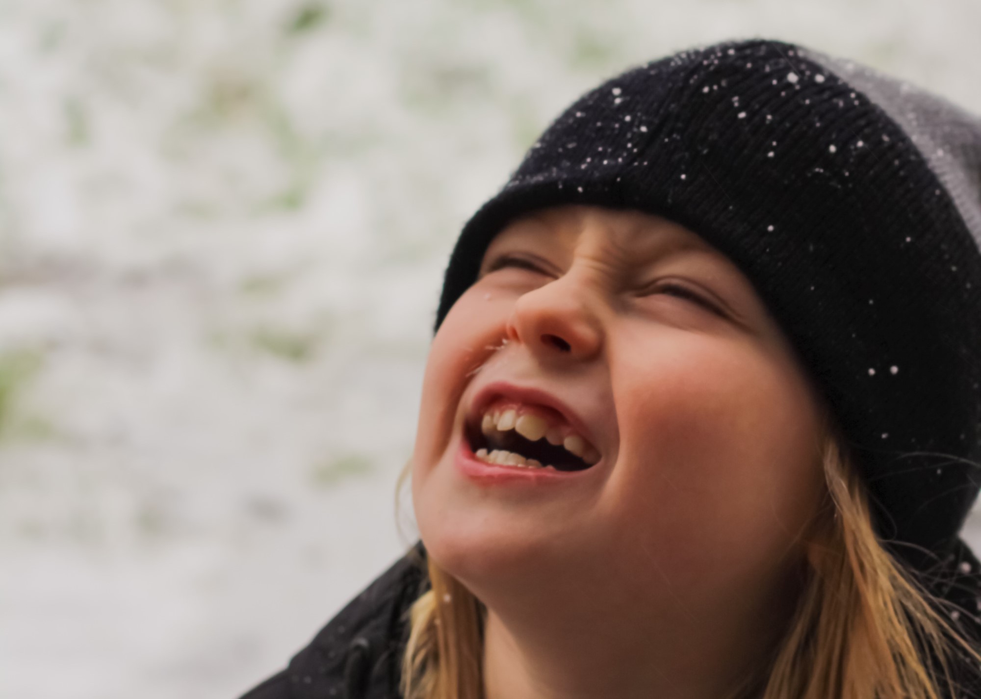 Jente med lue som myser mot snø som daler ned fra himmelen