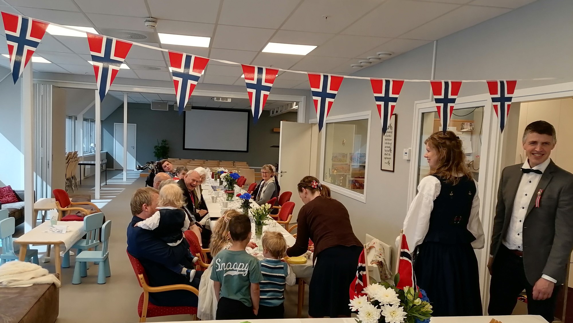 Bildet viser festglade mennesker rundt et pyntet bord klare til å spise frokost.