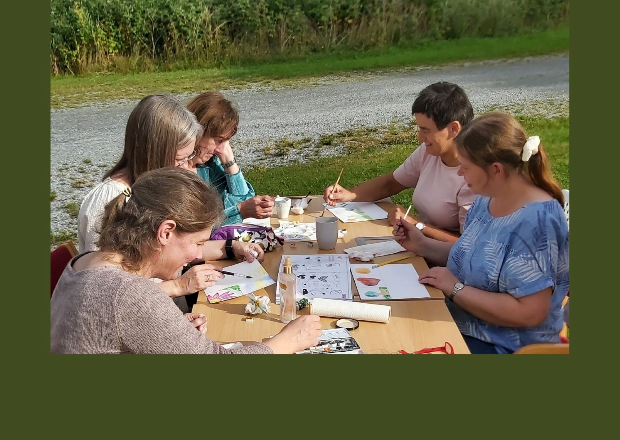 Damer sitter rundt et bord og maler akvarellbilder