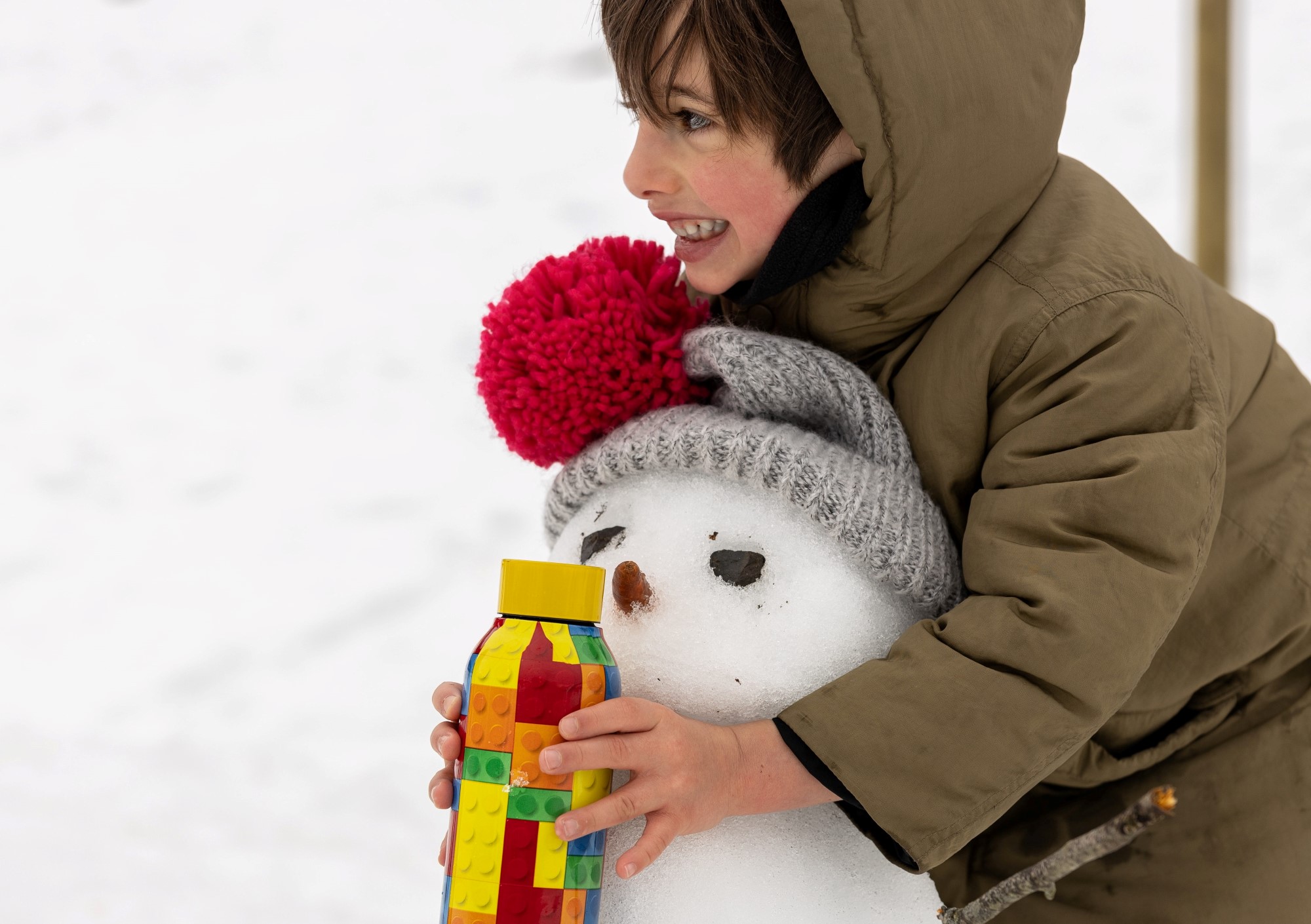 Gutt som holder rundt en snømann, og har en legoflaske i hånden.