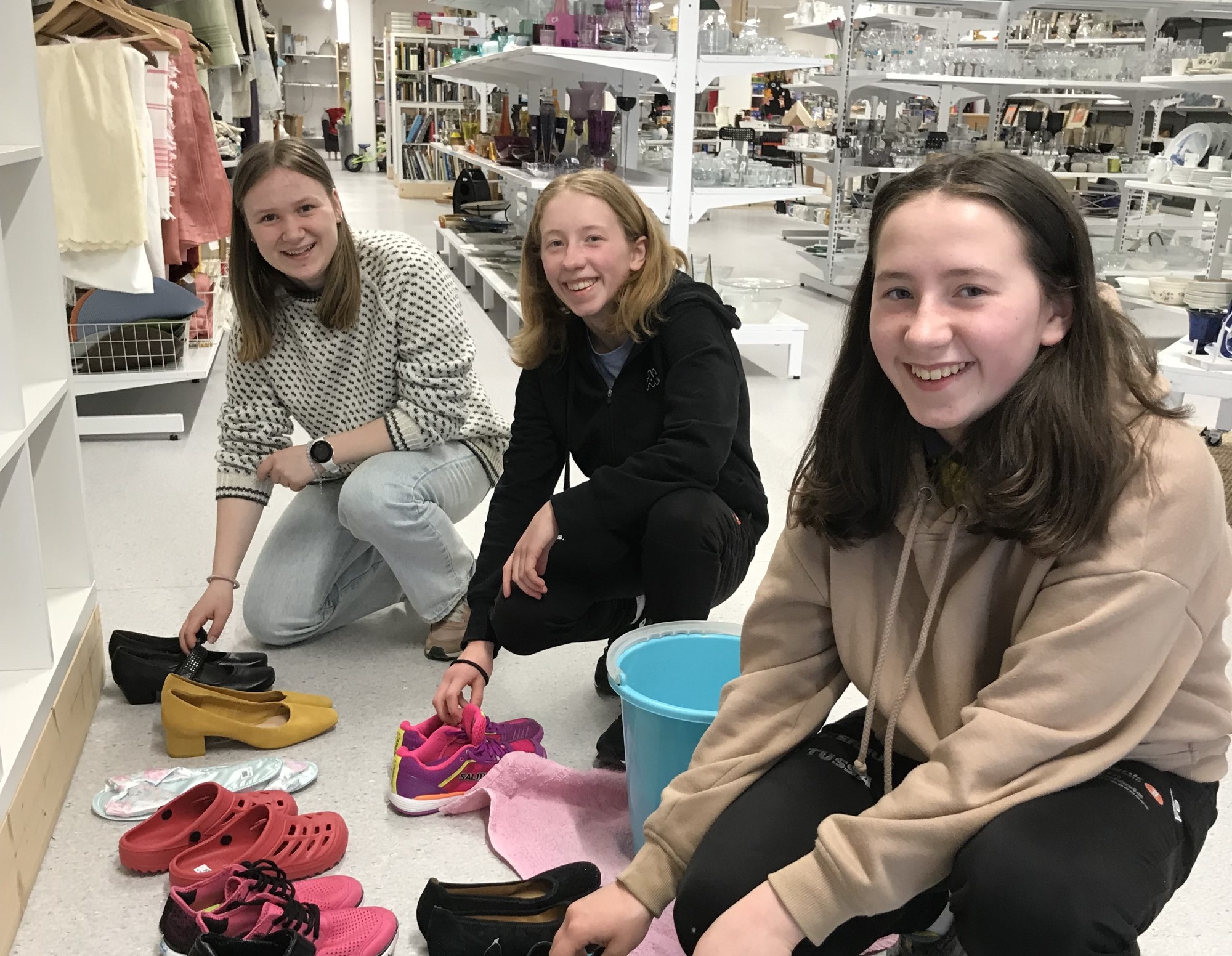 Tre jenter rydder i sko i gjennbruksbutikken