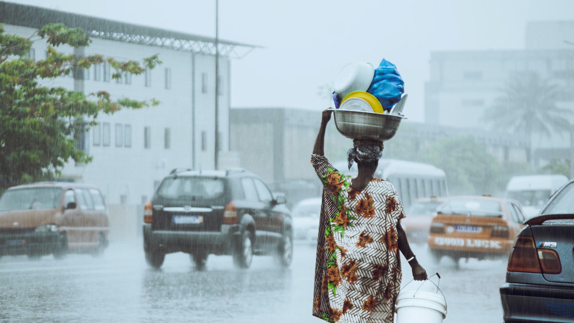 Afrikansk kvinne bærer stor bolle på hodet i regnvær