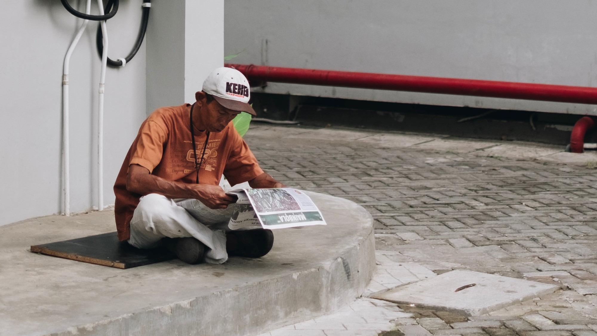 Asiatisk mann sitter på fortauet og leser avisen
