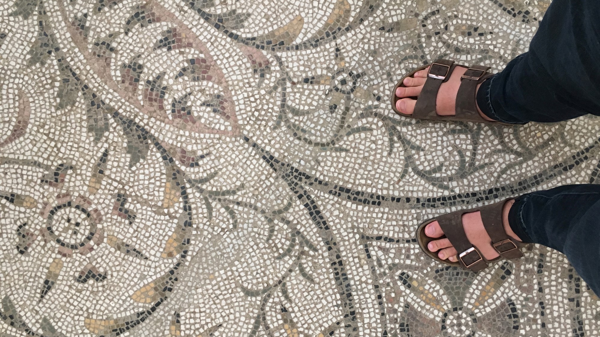 Føtter i sandaler på mosaikkgulv