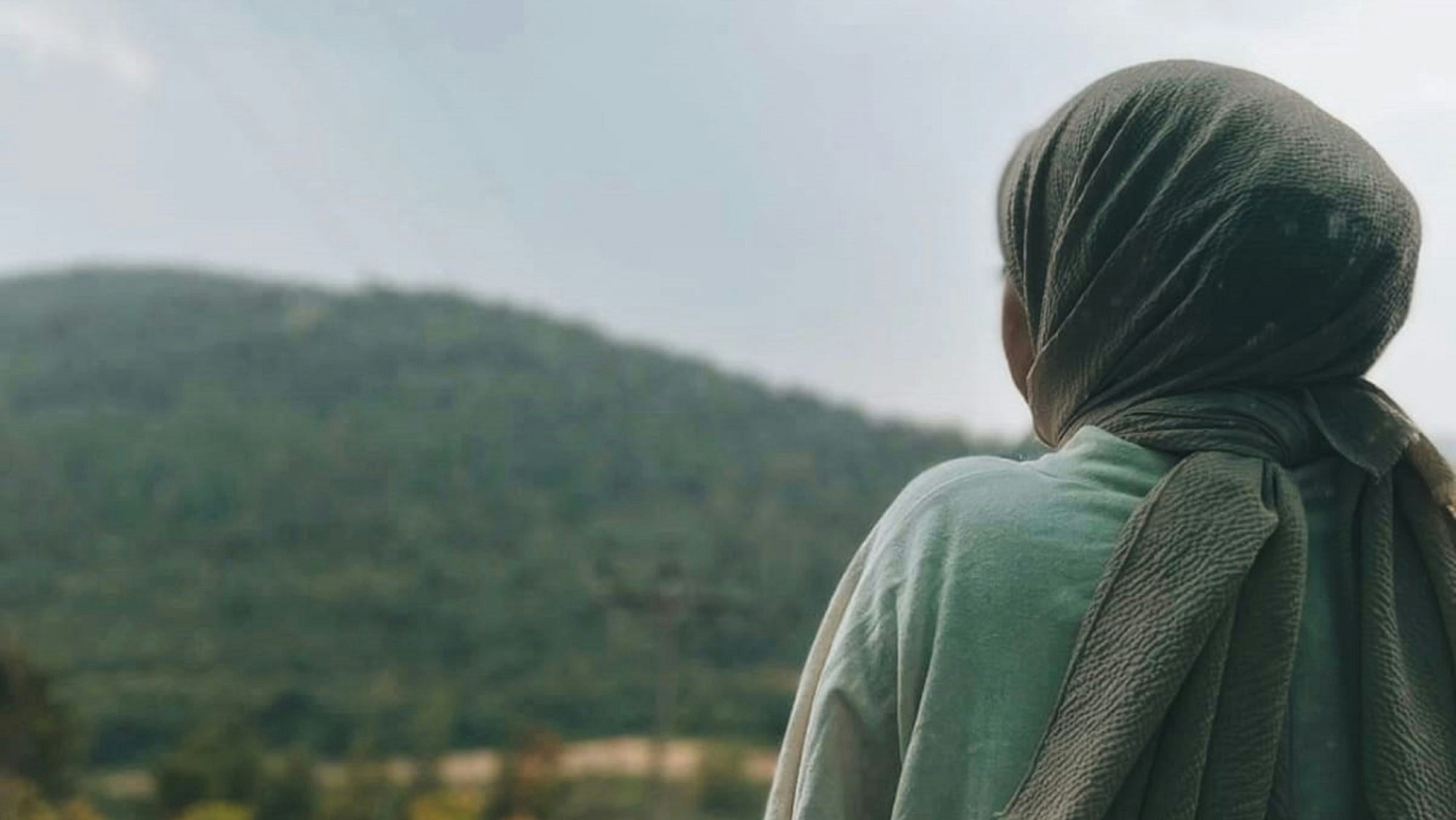 Kvinne med hodeslør ser utover diffust landskap