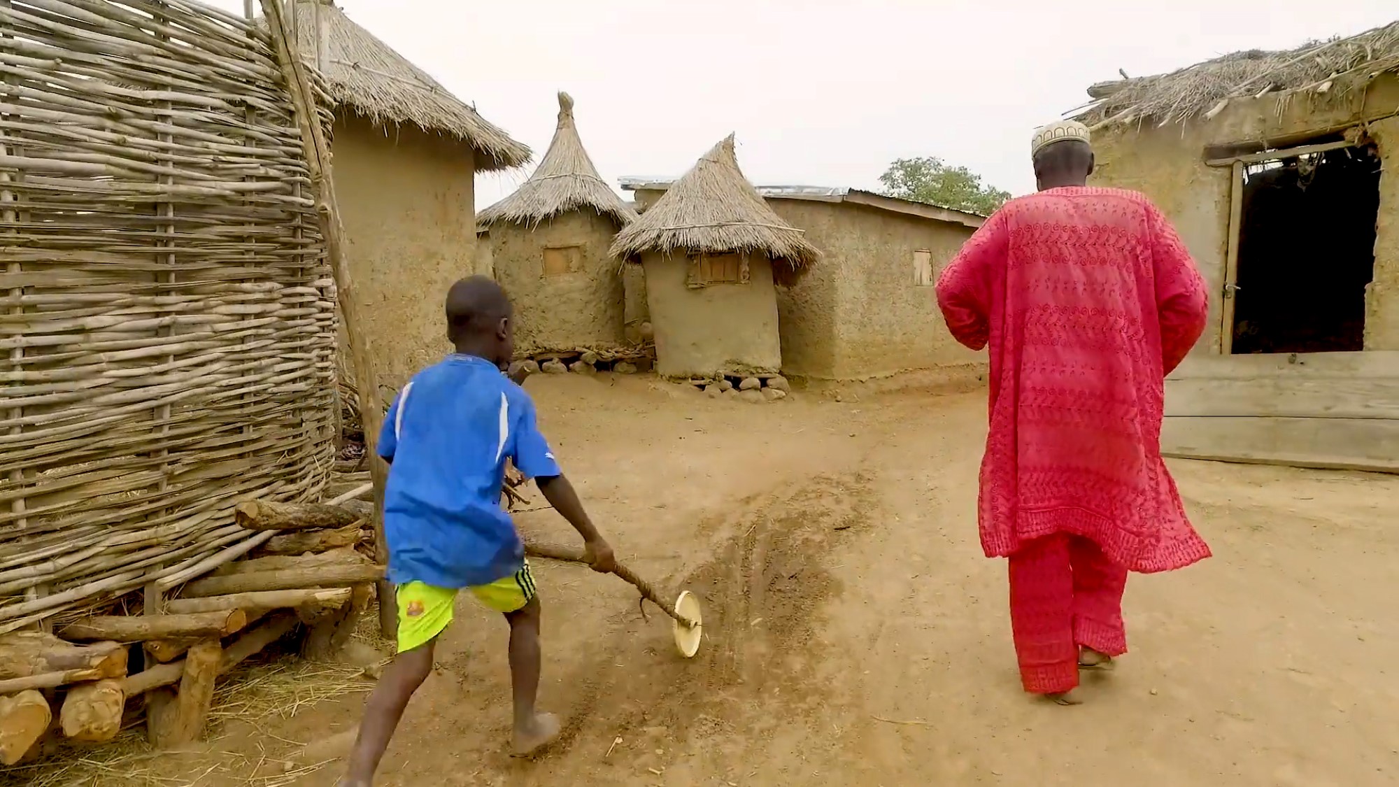 Eldre mann og gutt går mellom jordhytter i landsby