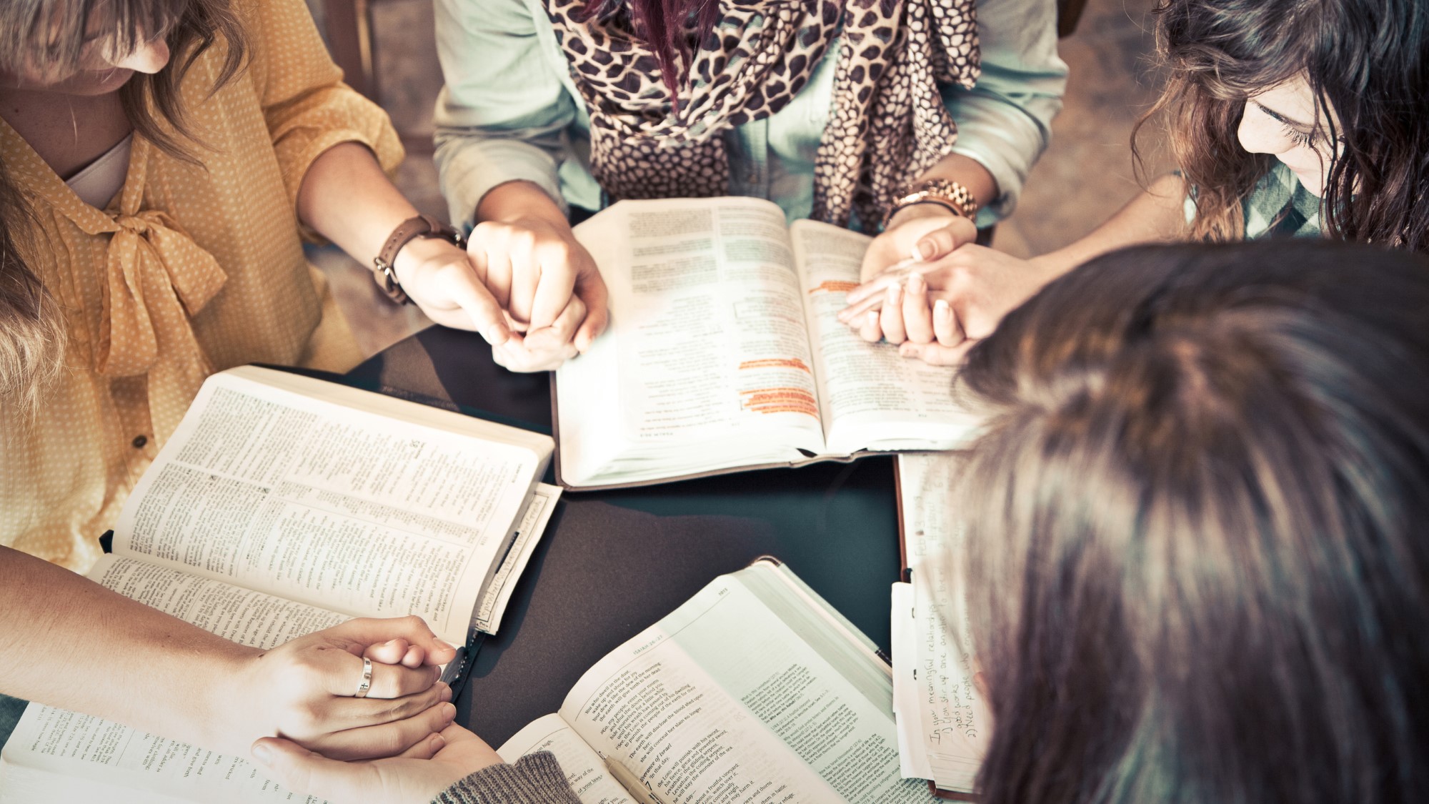 Kvinner holder hender i bønn over åpne bibler