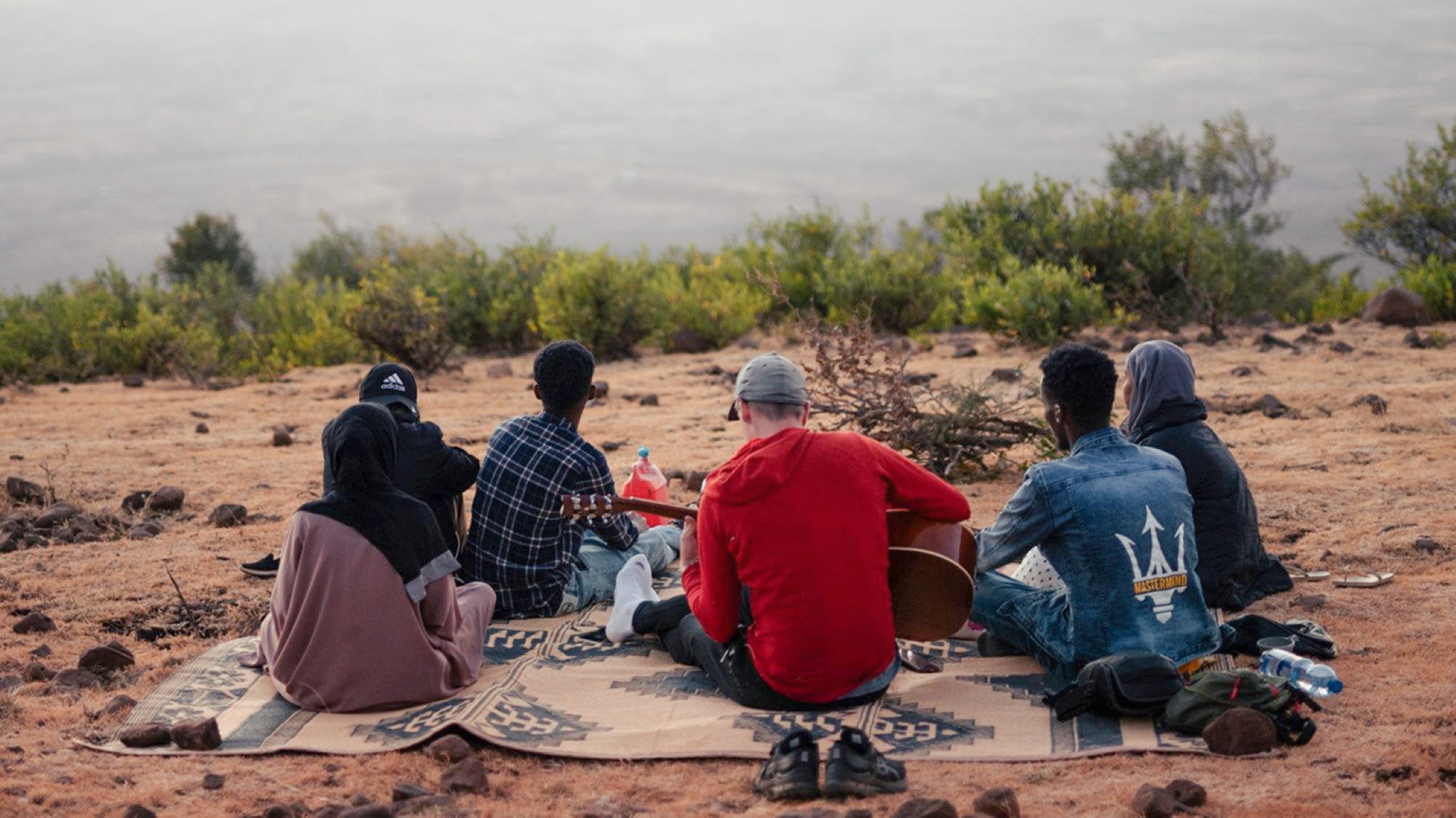 Norsk ungdom sitter i afrikansk landskap og spiller gitar med lokal ungdom